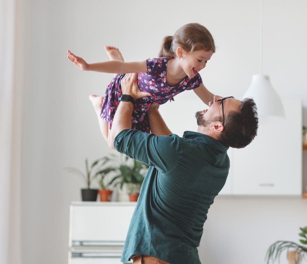 Parent lifting child in a bright living room at Gradience townhomes by Apna Group, featuring modern decor and a cozy atmosphere in Central Gordon, Langley, BC.